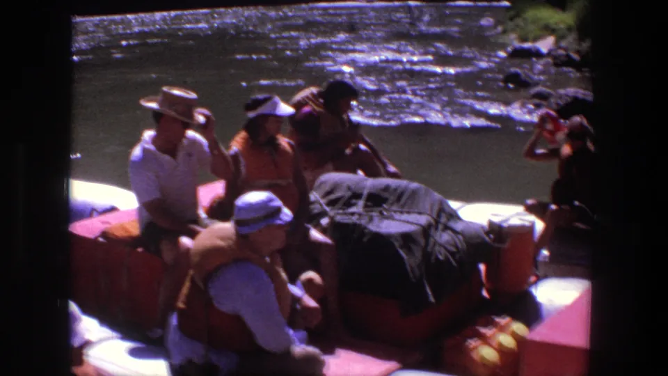 1969 Utah home-movie frame of rafters in life vests seated with gear in a white inflatable boat.