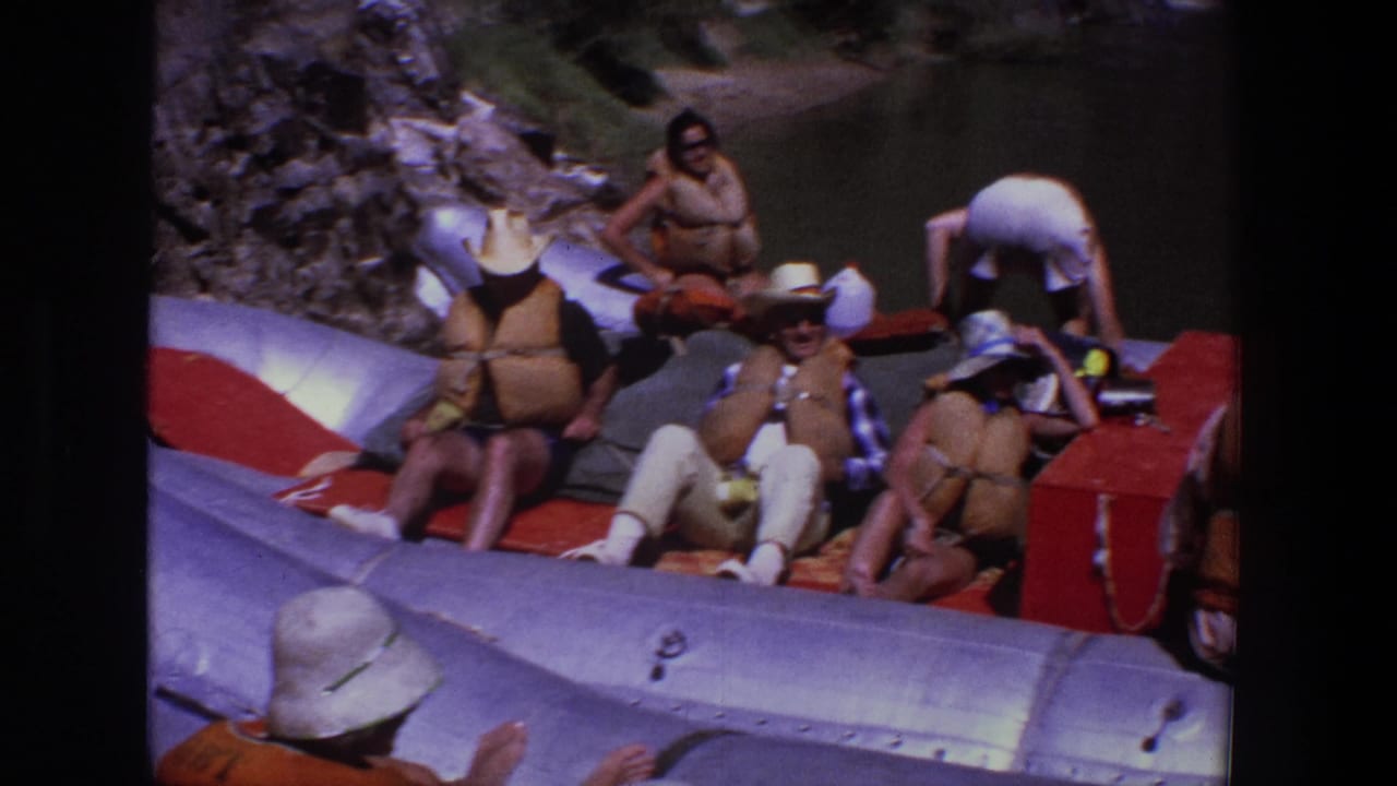 Group seated in a silver raft while one man bends near the red raft section.