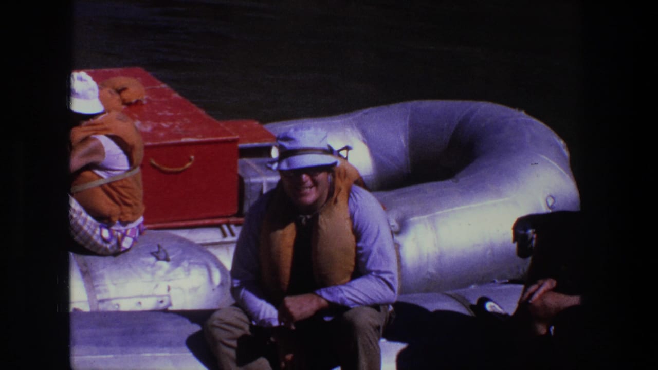 People in life jackets sit on a large inflatable raft beside a red storage box.
