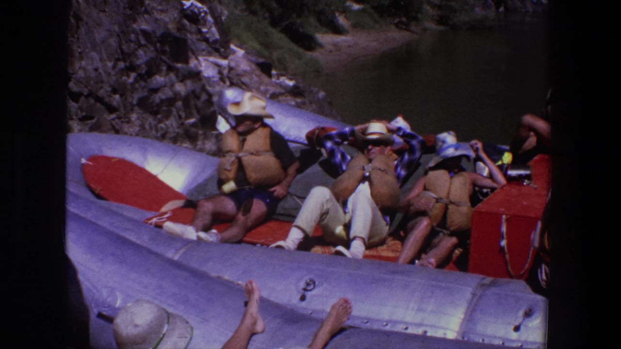 Several people lounge on red cushions inside an inflatable raft on calm water.
