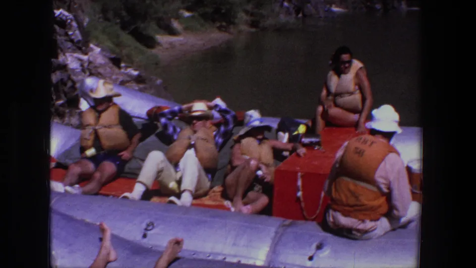 Late-1960s Utah raft outing with passengers resting in orange life jackets and a boat handler nearby.