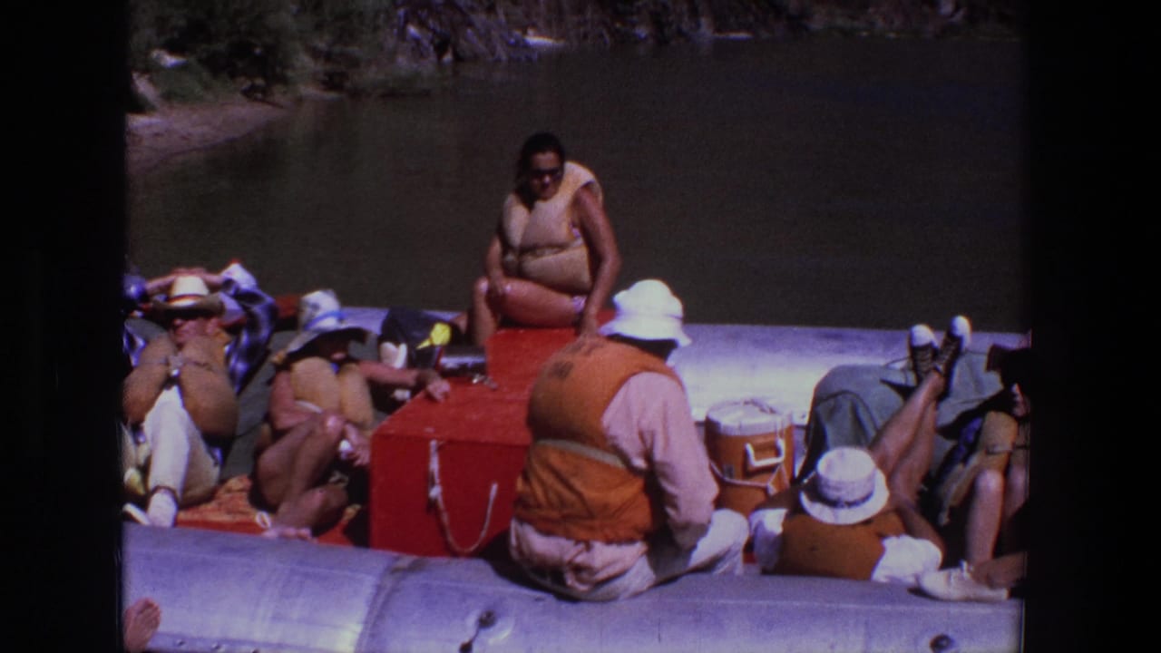 Group members sit and recline on a raft beside red and white coolers.
