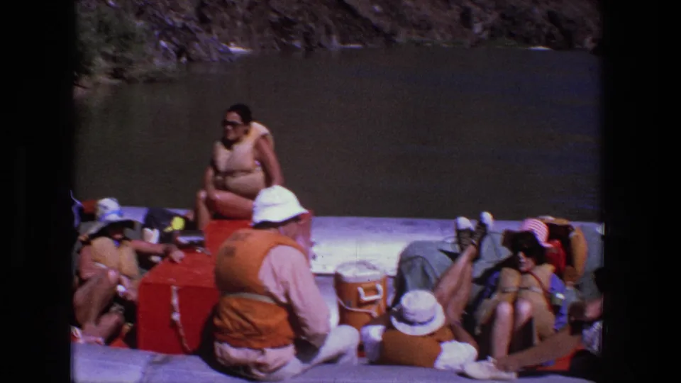 1969 Utah river footage shows adults lounging across an inflatable raft, with orange life vests, hats, a red cooler, and a white cooler visible.