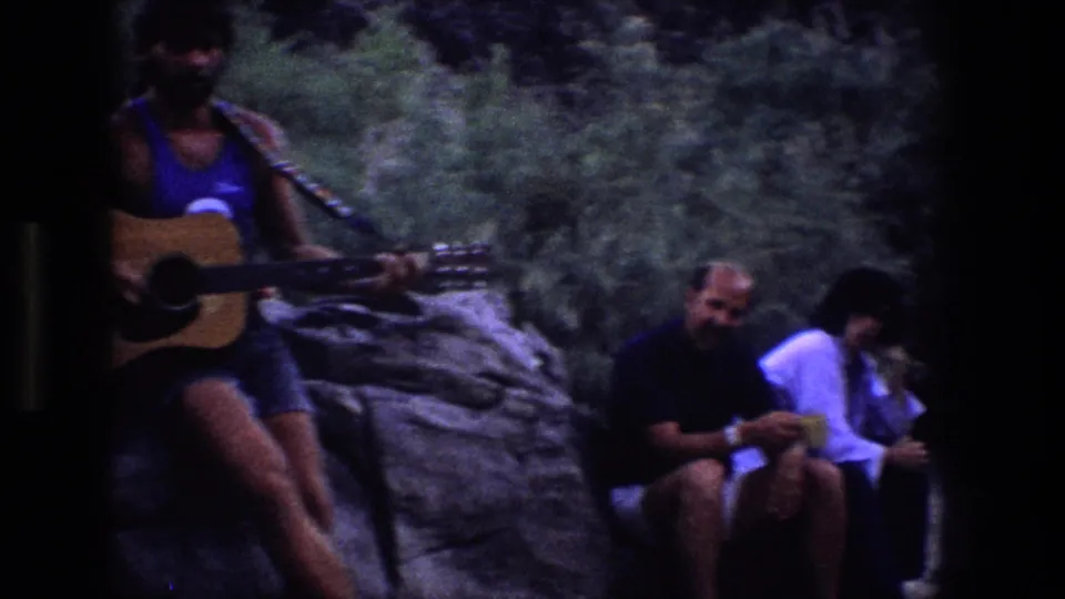 1969 Utah outdoor gathering with a guitarist at left and seated companions on rocks in a wooded setting.