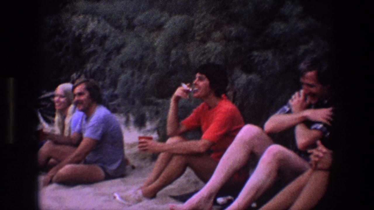 Group seated on sand, with a man in a red shirt drinking from a cup.