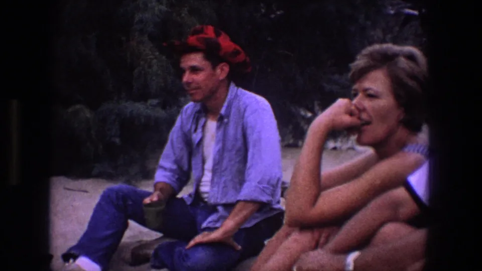 The frame shows a seated man in a red bandana and a woman in the foreground, part of a casual 1969 Utah outdoor gathering.