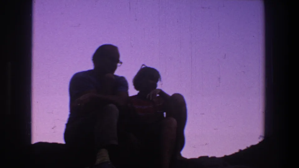 Two adults sit close together in silhouette against a pale purple backdrop in the same 1969 Utah home-movie clip.
