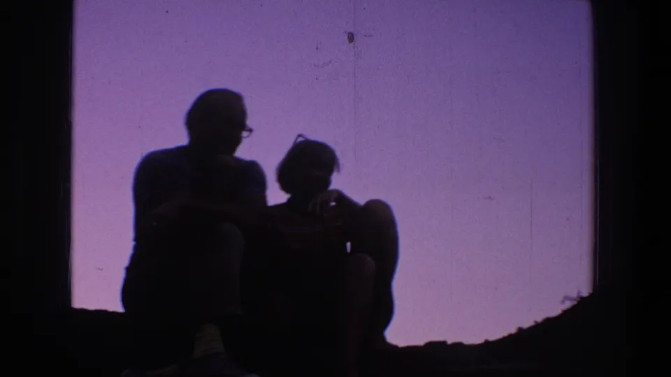 The seated pair remains in silhouette, with one figure wearing glasses, against a purple-lit backdrop in the 1969 Utah 8mm footage.