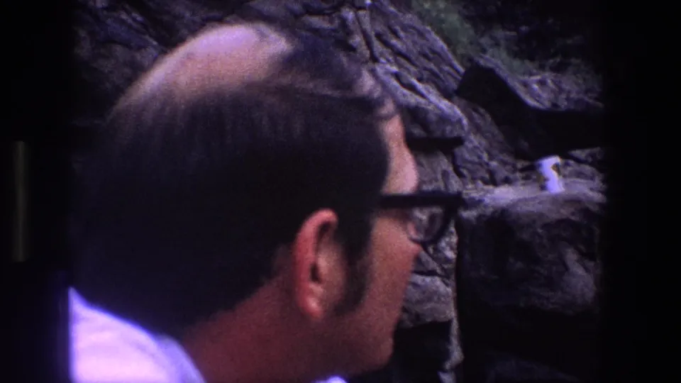 A man in glasses is seen in profile beside a rocky Utah cliff, facing a small pale bird perched near the rock surface.