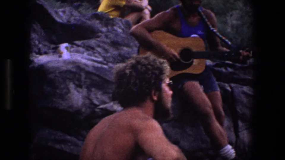 Young adults relax on rocky terrain in Utah, with one person in blue clothing holding and playing an acoustic guitar.