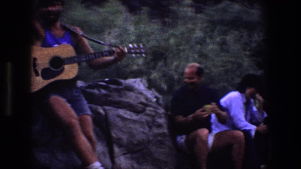 1969 Utah 8mm frame showing a man with an acoustic guitar seated on a rock while nearby friends sit in shade by sand and rock.