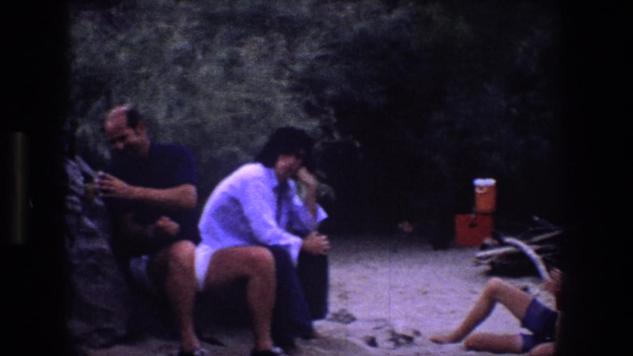 Adults seated by a rock wall with a cooler and a childlike seated figure partly visible at right.
