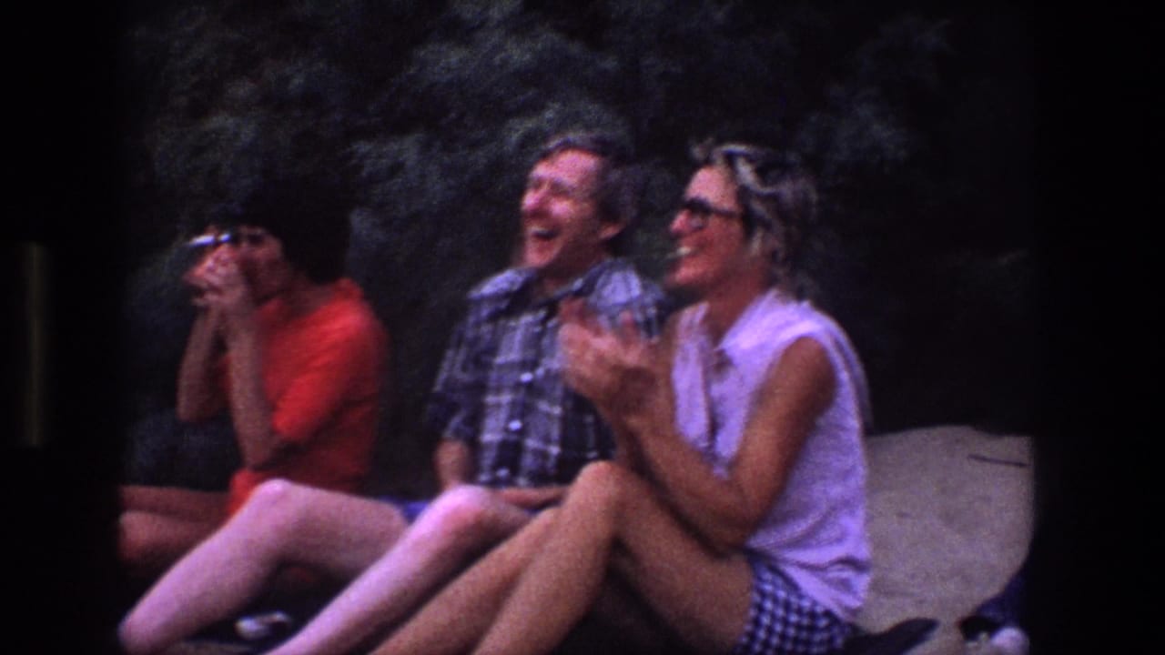 Three adults seated outdoors, laughing and watching something off camera.