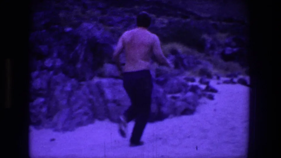 A shirtless man in dark pants runs away from the camera along a rocky Utah path bordered by shrubs and rough terrain.