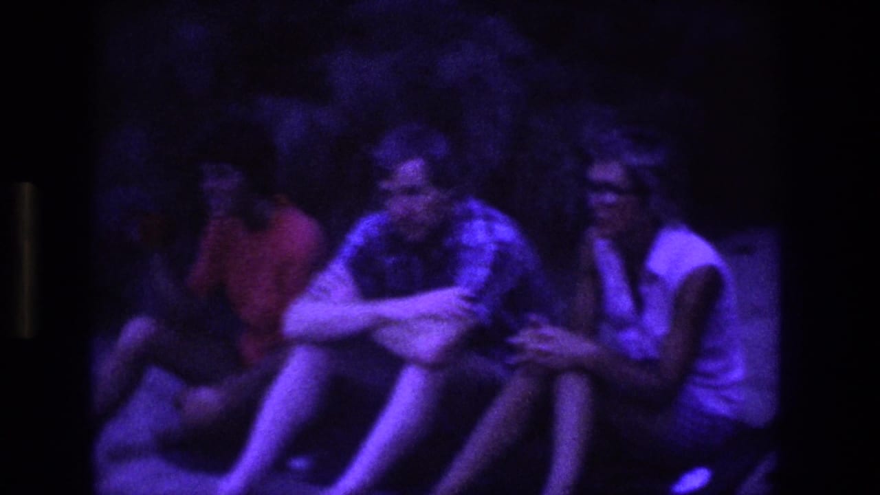 1969 Utah 8mm frame showing young adults sitting close together on grass under a strong purple glow at night.