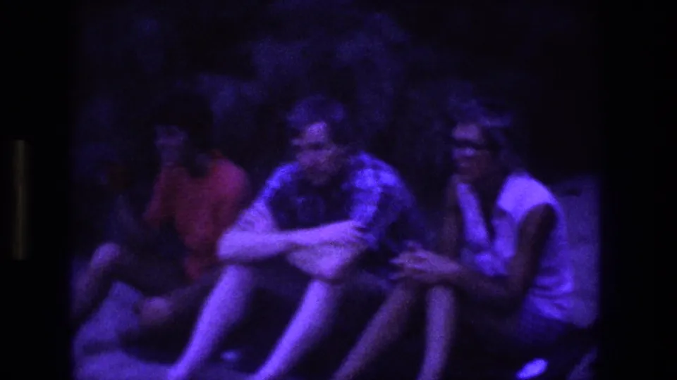 1969 Utah 8mm frame showing young adults sitting close together on grass under a strong purple glow at night.