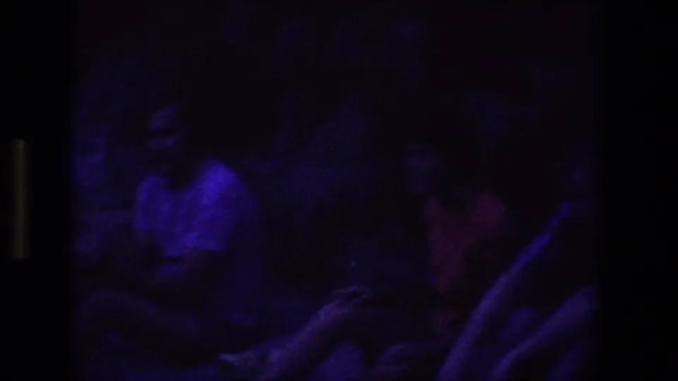 Low-exposure 8mm frame from Utah in 1969 with seated young adults barely visible under purple lighting.