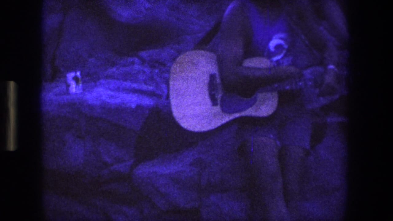 Acoustic guitar and seated young man near textured rock walls.