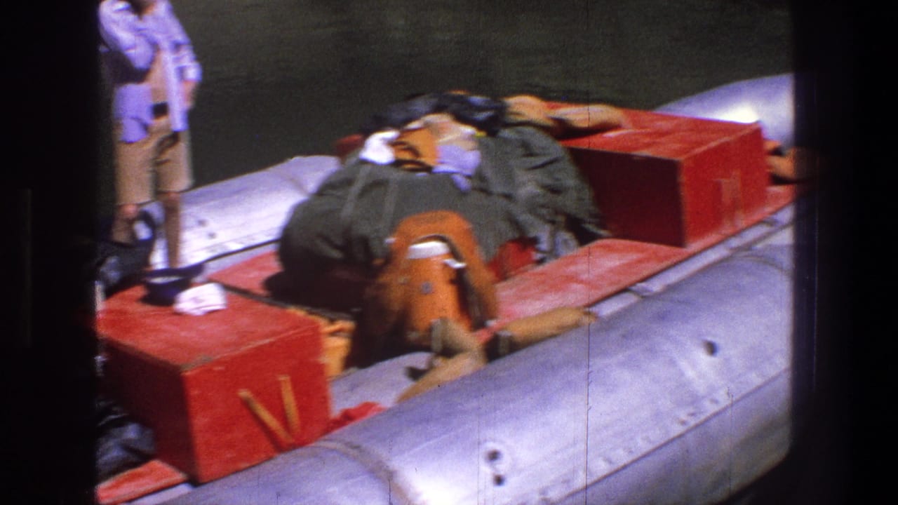 1969 Utah home-movie frame showing a woman near a heavily loaded inflatable raft with red boxes and camping gear by the river.