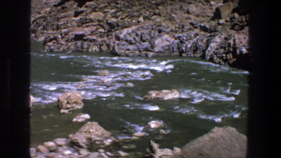 Utah river view from 1969 home-movie footage, showing choppy water, rocks, and the lower edge of a loaded raft near shore.