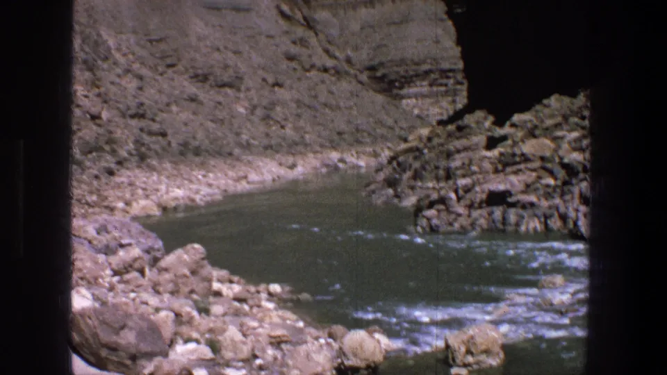 1969 Utah 8mm frame showing a river bend below steep, dry canyon walls and dark film gate edges.