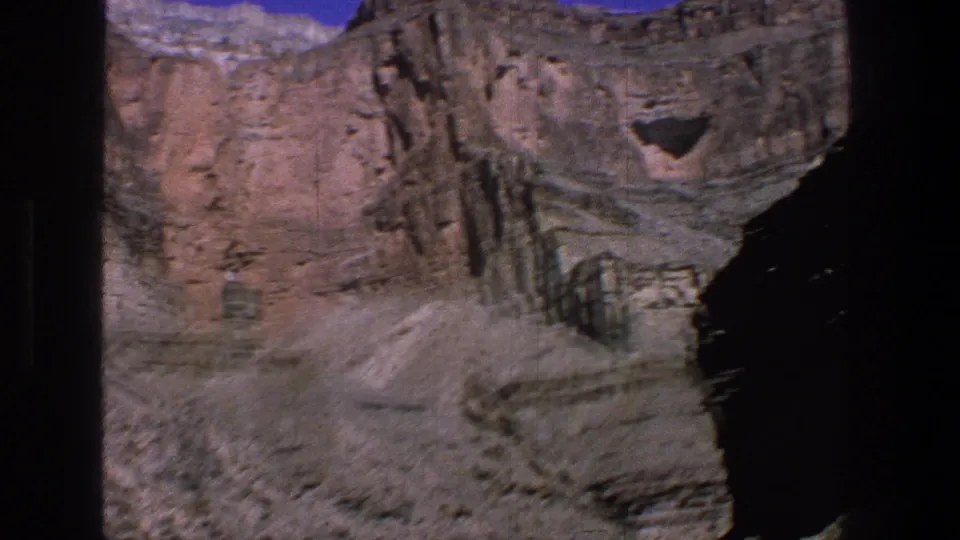 1969 Utah 8mm frame showing steep canyon walls, a pale dry slope, and the river corridor partially visible at the bottom.