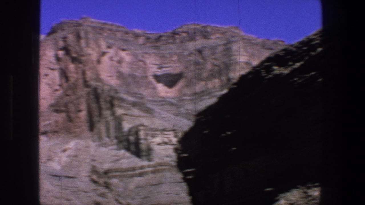 Layered canyon cliffs under a blue sky with dark vertical frame edges.