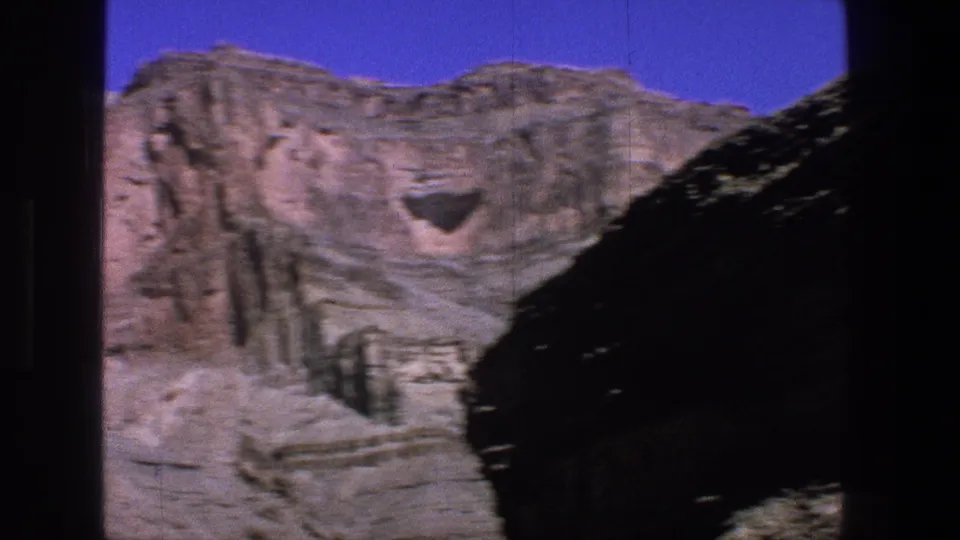 1969 Utah 8mm frame showing sunlit layered canyon rock and blue sky, partly obscured by dark foreground edges.
