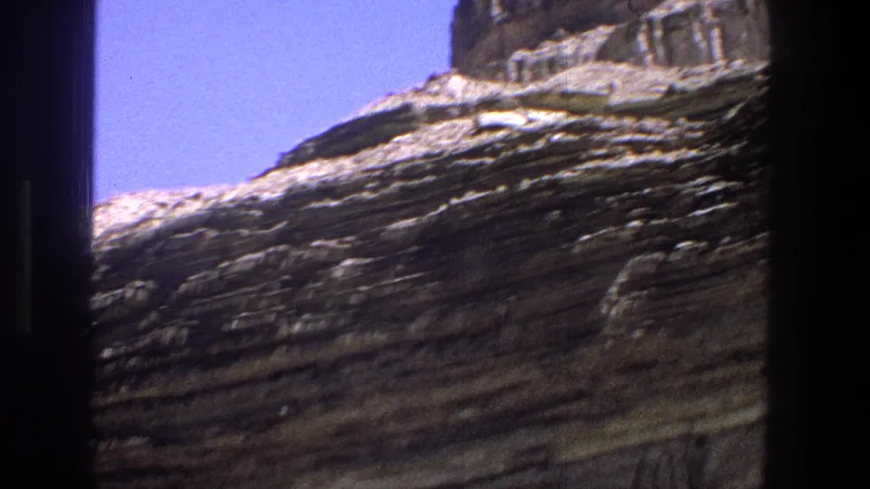 1969 Utah 8mm frame showing a broad layered rock slope, cliff textures, and a narrow strip of clear sky.