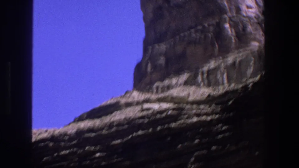 1969 Utah 8mm frame with a tall canyon wall or rock column, lower ledges, and saturated blue sky.