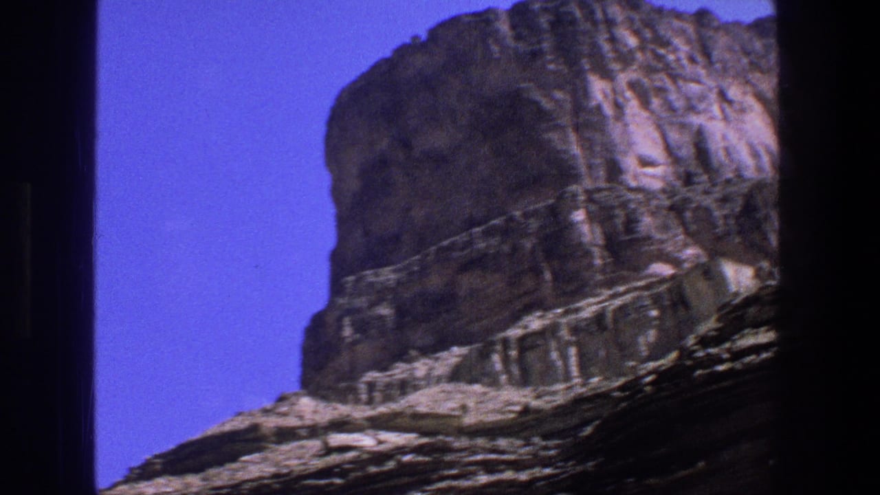 Layered rock formation rising under a clear blue sky with dark film edges.