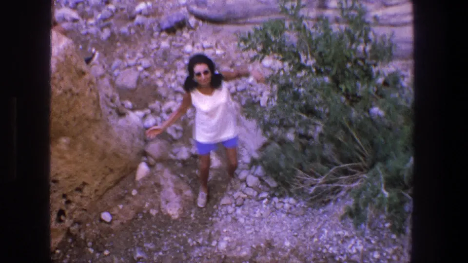 In supported 1969 Utah home-movie footage, a woman stands in a rocky riverbed below the handheld camera.