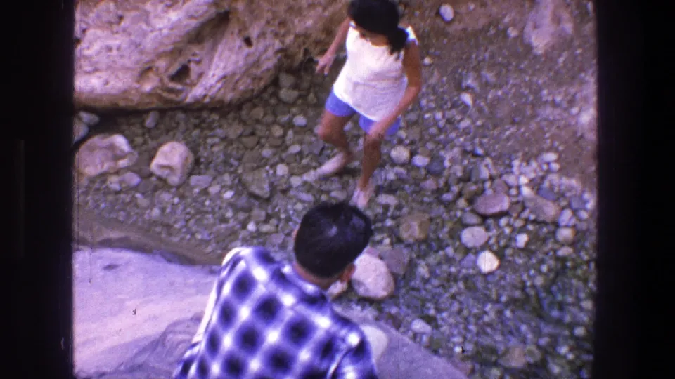 The woman steps through stones toward the man below the camera in the 1969 Utah outdoor home-movie footage.