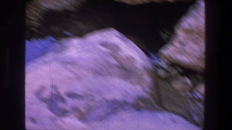 A handheld, blurred frame shows pale rock and a dark recessed area as the camera shifts in the rocky Utah setting.