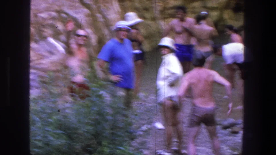 Adults in swimwear, hats, and sunglasses gather near a canyon pool in 1969 Utah home-movie footage.