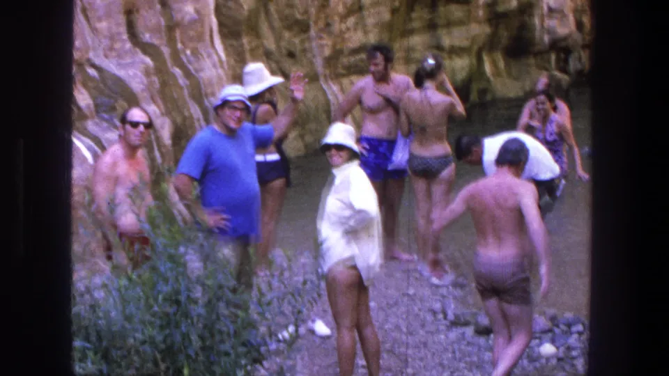 Adults wade and pause in a shallow Utah canyon pool, with layered rock walls behind them.
