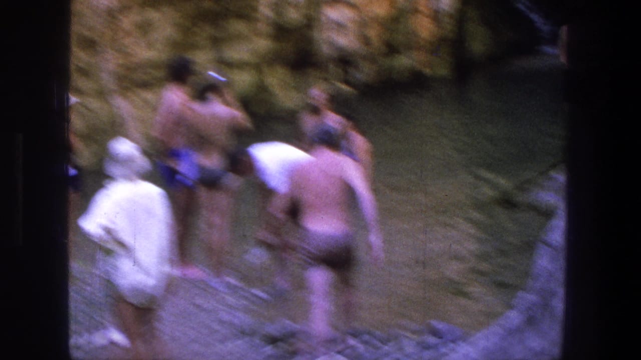 Several swimmers stand and bend near the water in a rocky canyon pool.
