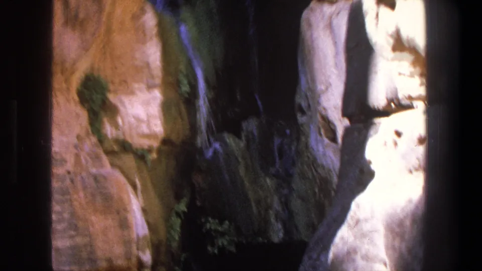 The frame looks into a shaded canyon creek passage in Utah, with a swimmer partly obscured by rock and film blur.