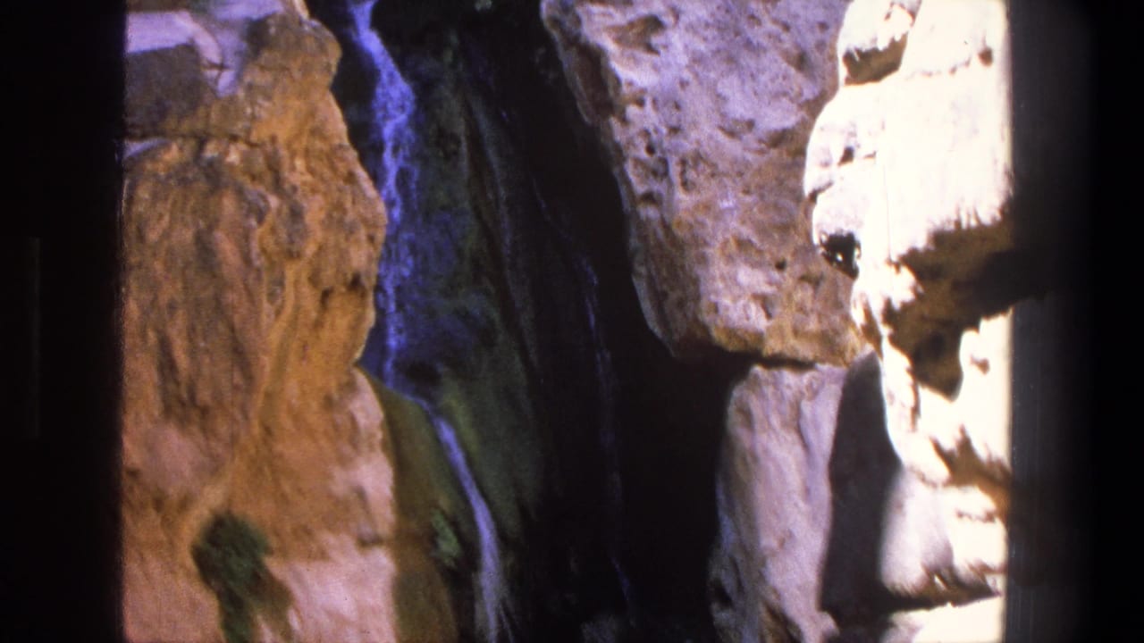 Narrow waterfall running beside rugged sunlit canyon rocks.