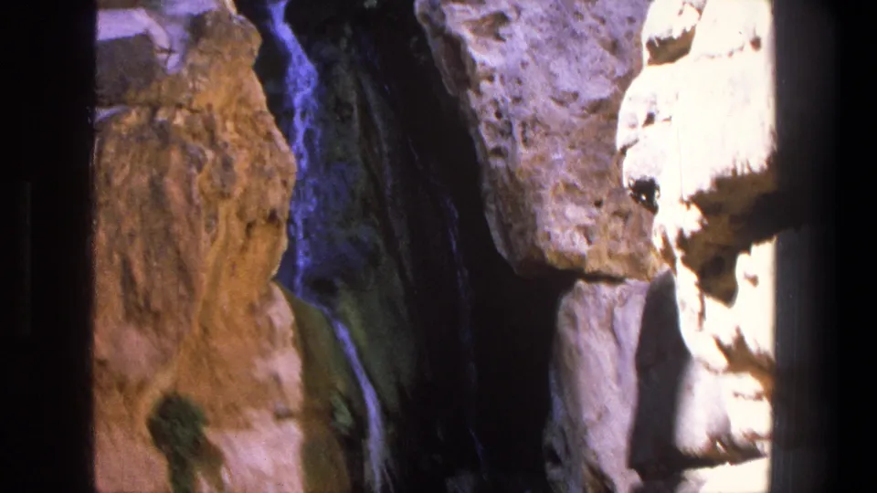 1969 Utah 8mm frame showing a slim waterfall and textured canyon rock in mixed sun and shadow.
