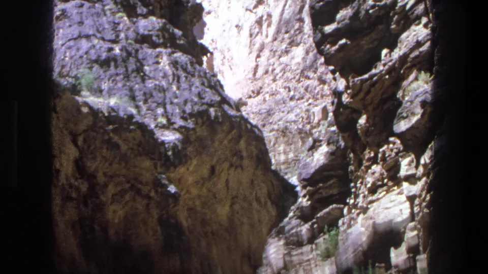1969 Utah 8mm frame showing a shadowed waterfall thread between large textured canyon rocks.