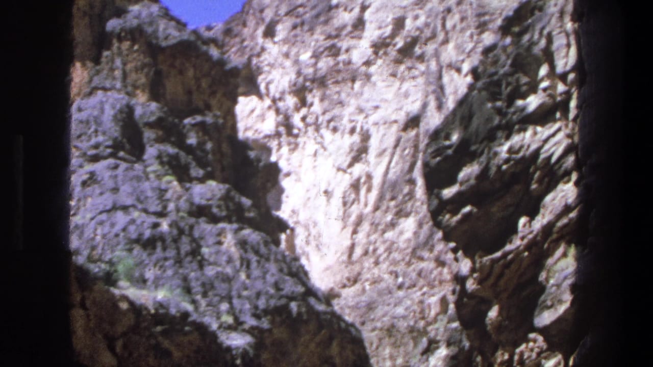 1969 Utah home-movie frame showing pale canyon rock, dark shadowed water, and a strip of blue sky above.