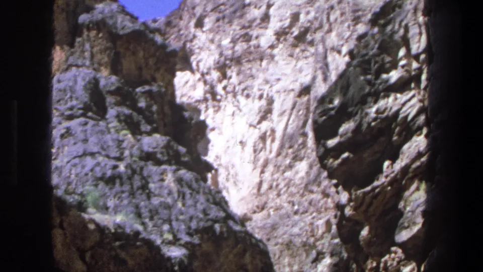 1969 Utah home-movie frame showing pale canyon rock, dark shadowed water, and a strip of blue sky above.