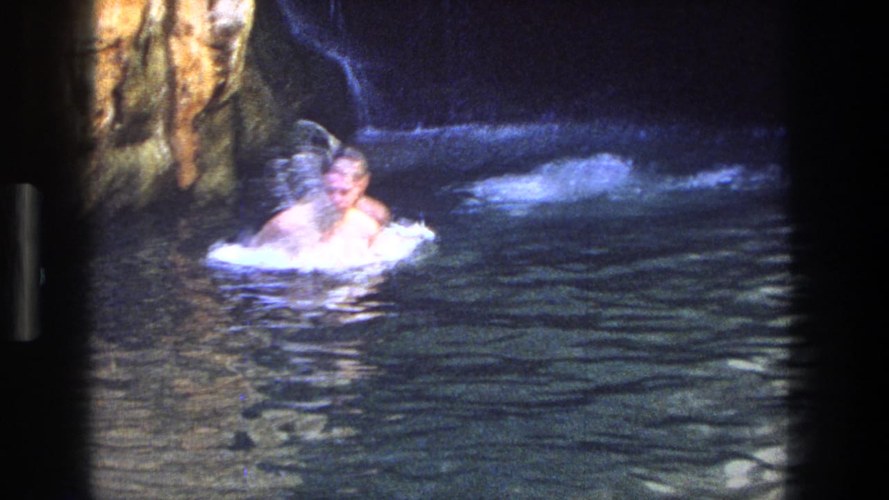 People swimming in a dark rocky pool beside canyon walls.