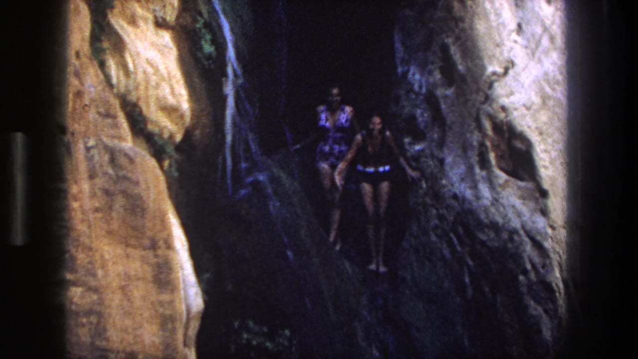 Two women in swimsuits stand in a narrow rocky canyon passage.