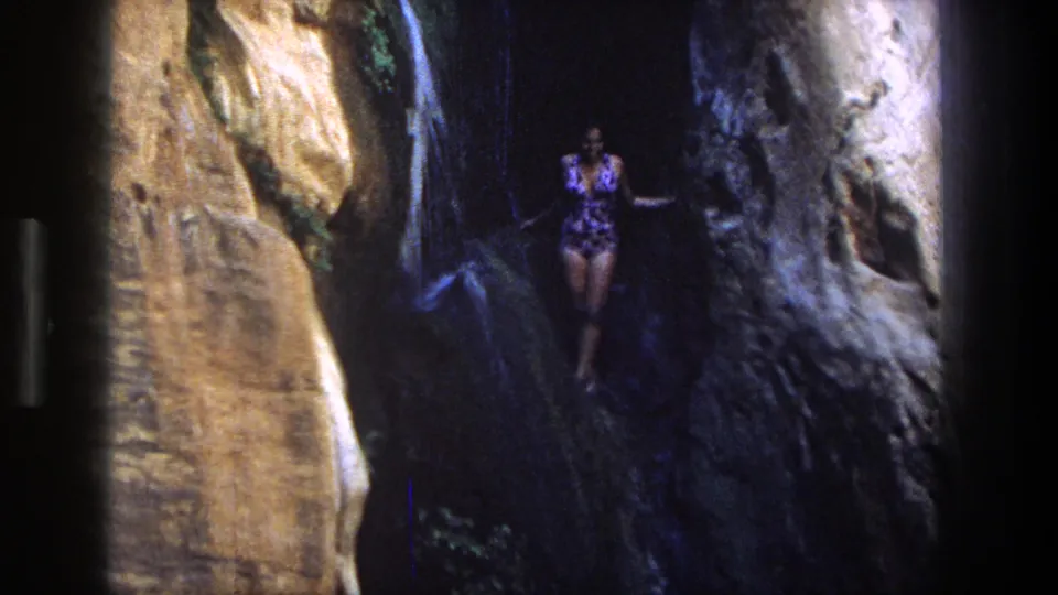 A woman in a patterned swimsuit stands against shadowed canyon rock in the Utah waterfall setting.