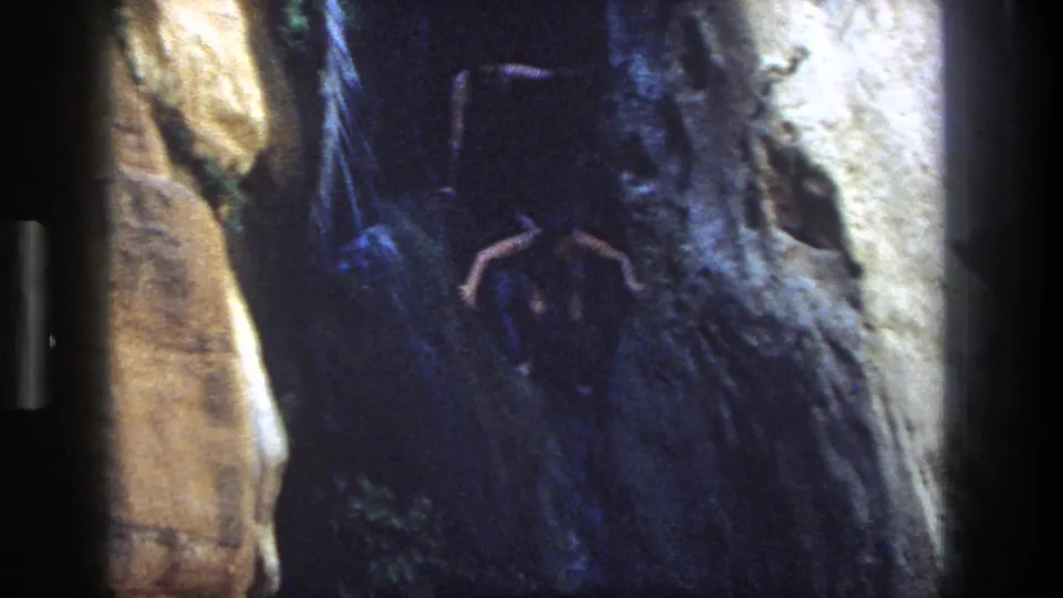 1969 Utah 8mm frame showing a man poised on a canyon rock ledge above dark water.