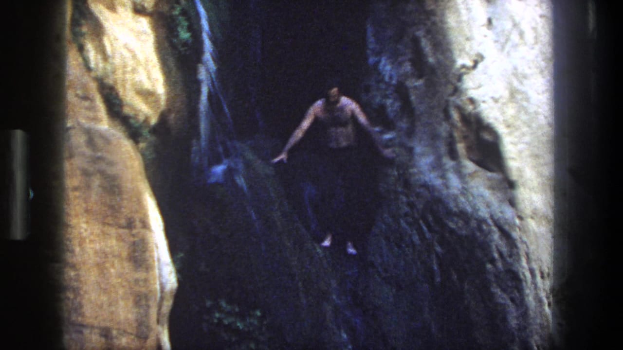 Man jumps from a high rocky ledge toward the pool below.