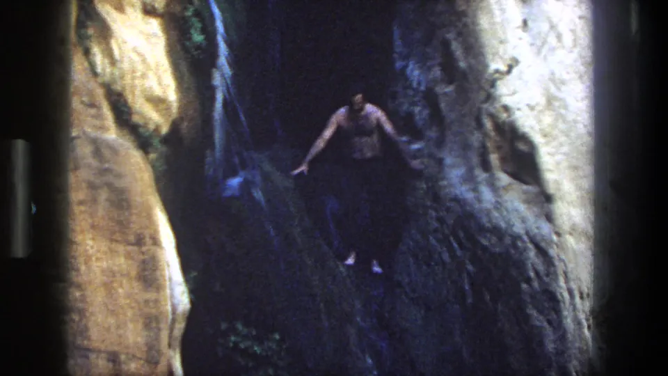 1969 Utah 8mm frame with a man mid-jump from canyon rocks into a dark waterfall pool.