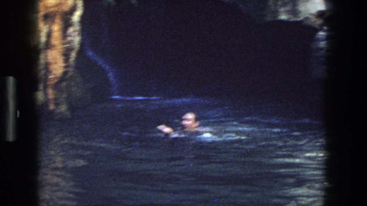 A swimmer moves through a dark rocky pool in archival 8mm footage from the Utah 1969 clip.